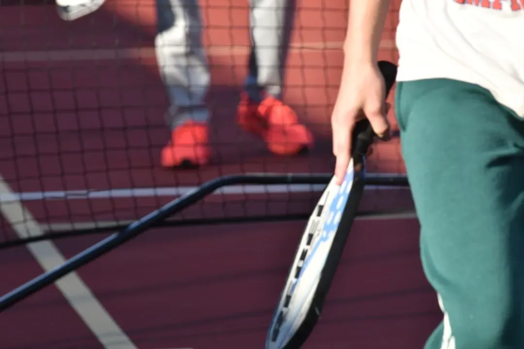 Pickleball player holding a paddle at the net on an indoor court, ready to return a shot