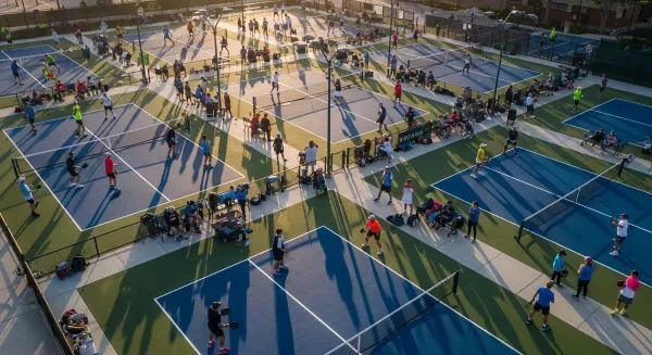 Aerial view of crowded pickleball courts at dawn with multiple packed courts and waiting players illustrating the court short