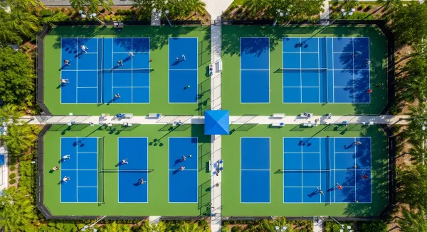 Aerial view of multiple outdoor pickleball courts with players actively competing, showing proper spacing, regulation nets, a